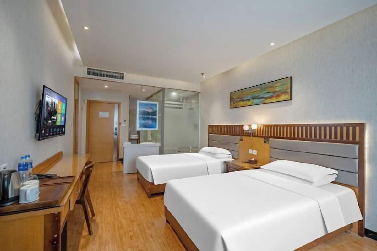 Een hotelkamer met twee bedden, een bureau met stoel, een televisie en een schilderij aan de muur.