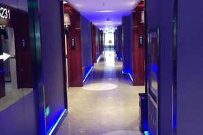 Un couloir d’hôtel avec un chemin rectiligne, des panneaux de signalisation et une poubelle.