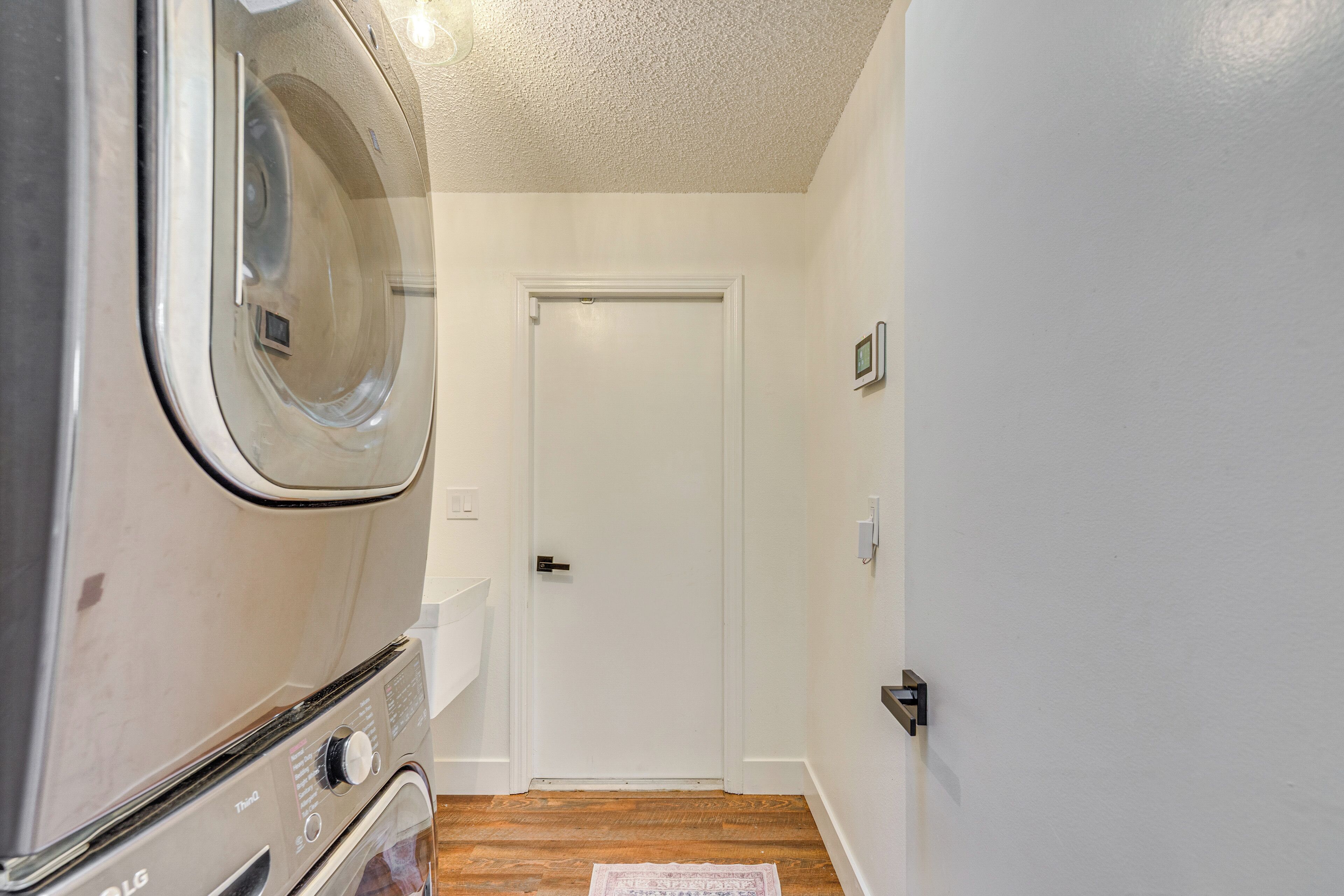 A laundry area with a washing machine, a door, and a wooden floor.