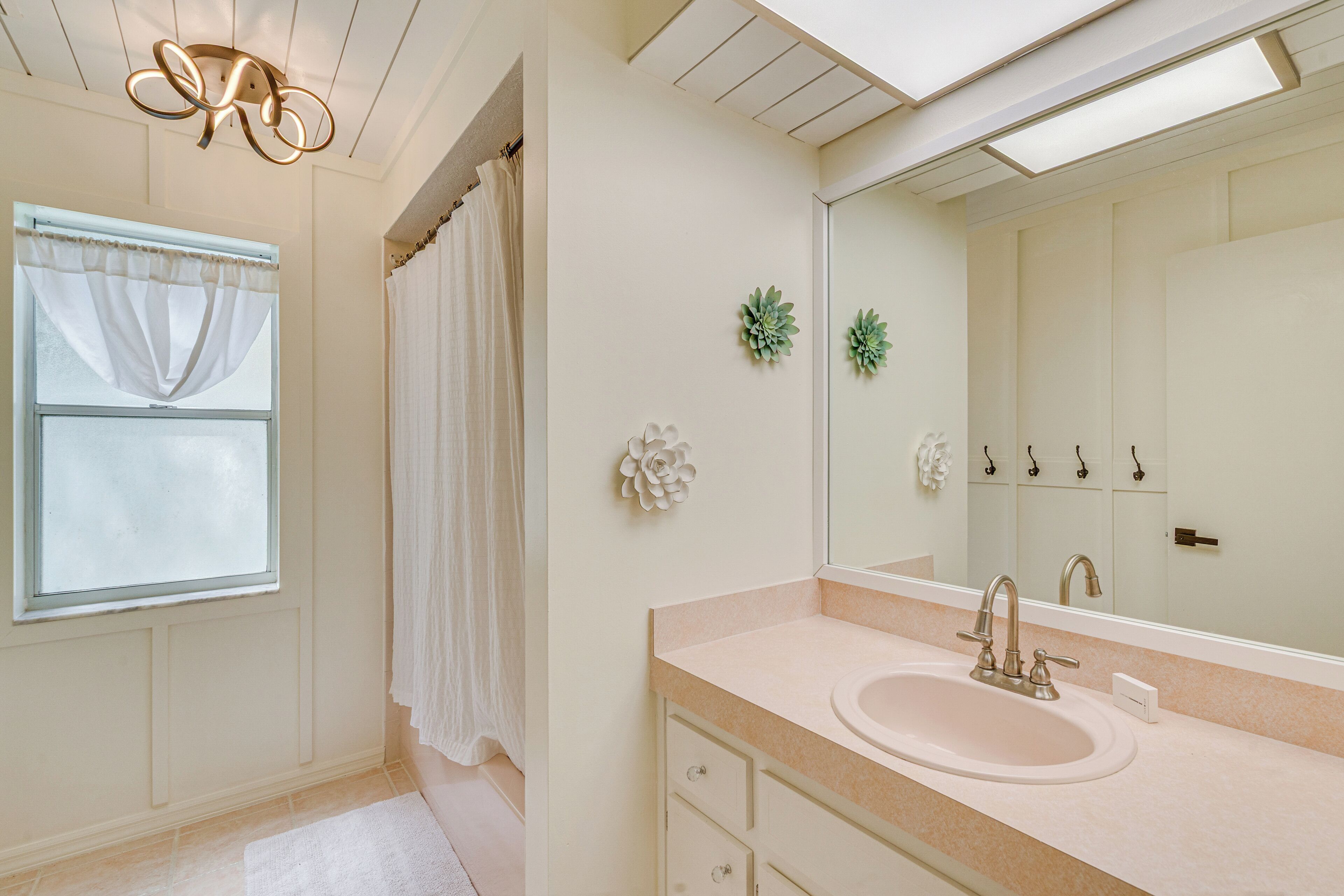 Une salle de bain avec un lavabo, un miroir et une fenêtre avec des rideaux.