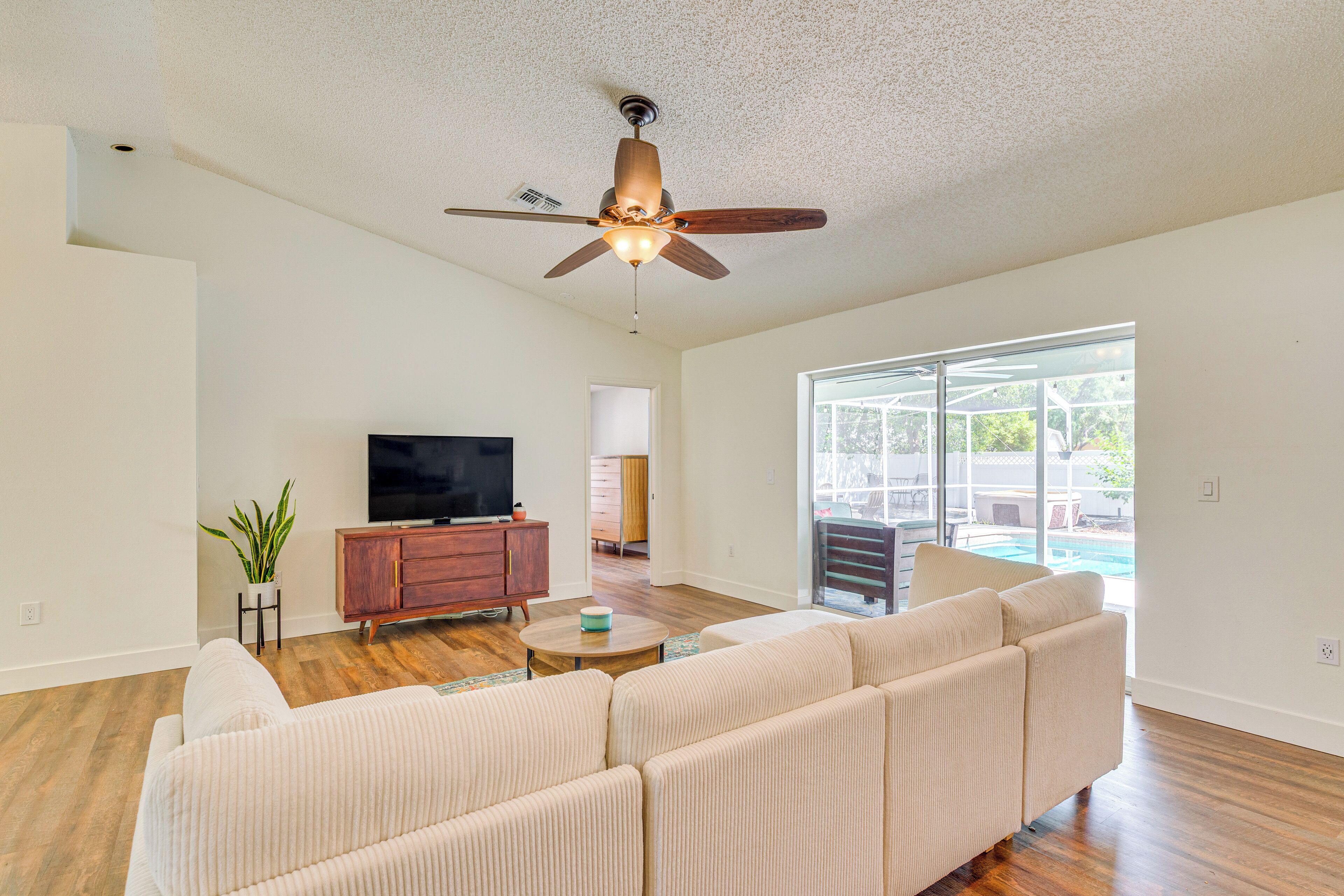 A spacious living room with a large sofa, a television, and a ceiling fan.