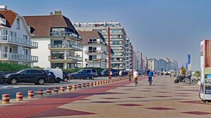 A coastal promenade with modern buildings, a bike lane, and parked cars. - Apartment in Seaside Bruges With Balcony (Knokke-Heist)