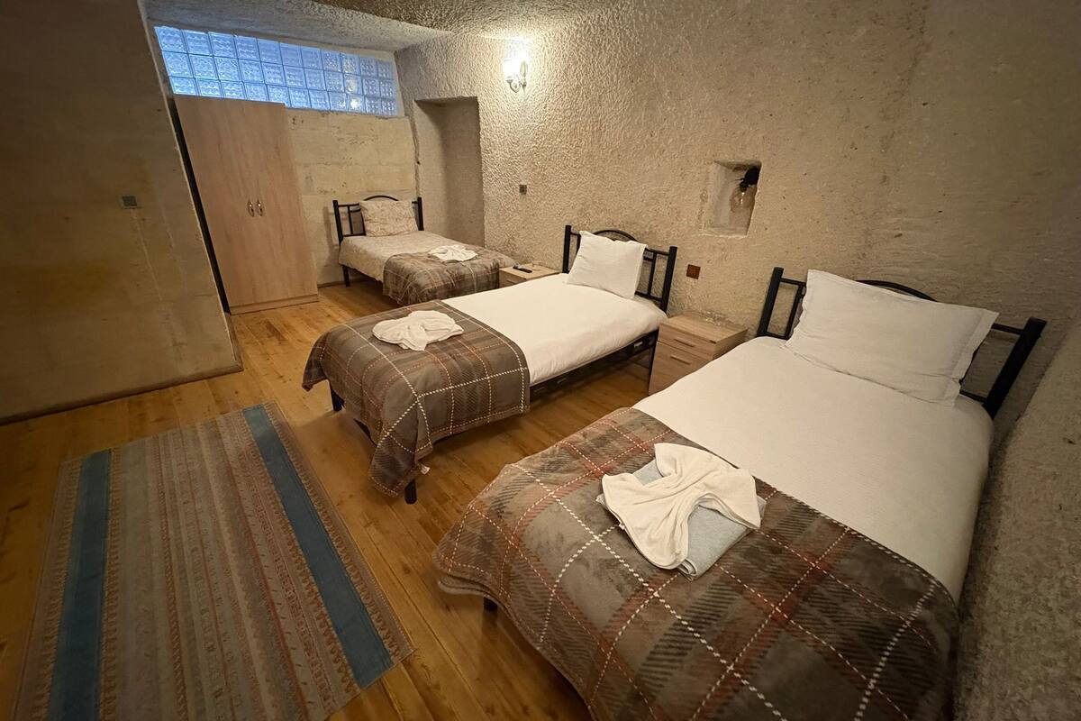 Una habitación con dos camas, piso de madera, ventana con vistas y una lámpara pequeña empotrada en la pared.