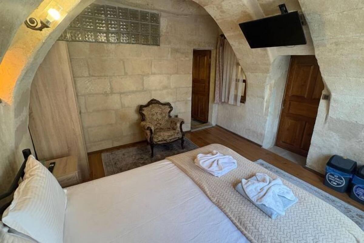 Un dormitorio con una cama, dos toallas, una silla y un televisor montado en la pared.