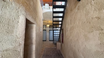 A narrow hallway with textured walls, a patterned rug, a ceiling light, and a view of a room with a closed door and a radiator.