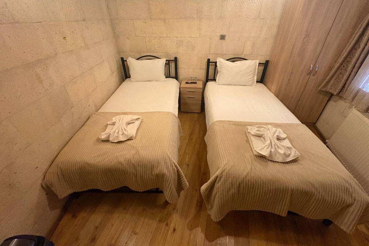 Una habitación con dos camas, cada una con almohada y manta, una mesita de noche y un armario de madera.