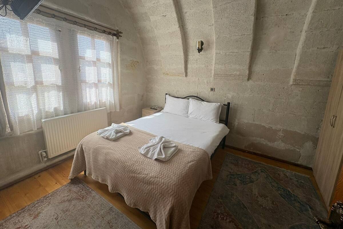 Un dormitorio con cama, ventana con cortinas, radiador y suelo de madera.