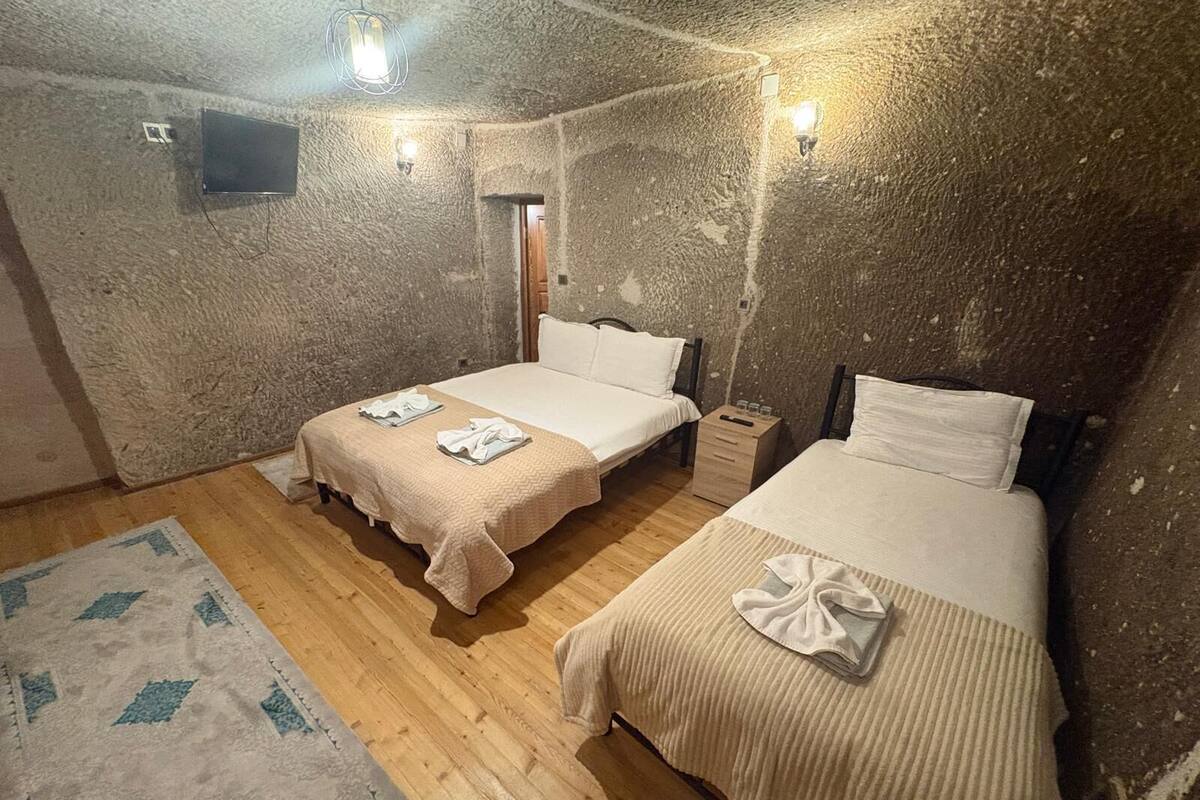 Una habitación con dos camas, suelo de madera, alfombra y televisor montado en la pared.