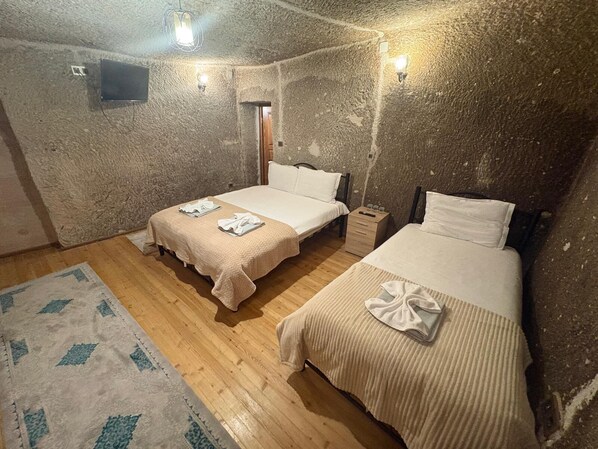 A room with two beds, a wooden floor, a rug, and a wall-mounted TV. - Ekoton Cave Hotel (Nevsehir)