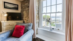 Un salón acogedor con sofá, televisión de pantalla plana, pared de piedra y ventana con vista a un lago.