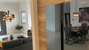Moderni olohuone, jossa on harmaa sohva, ruokailutila puupöydällä ja -tuoleilla sekä suuri peili, joka heijastaa huonetta.