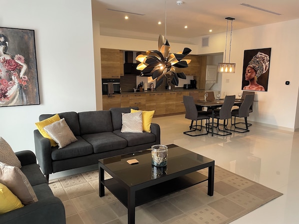 Una sala de estar moderna con un sofá oscuro, una mesa de centro de vidrio y una zona de comedor con una mesa y sillas.
