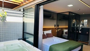 A modern hotel room with a large bed, a separate bathroom with a bathtub, and a glass shower enclosure. - Get One (Joao Pessoa)