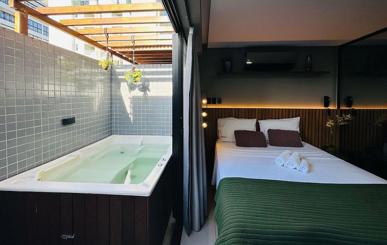 Et moderne hotelværelse med et stort badekar, en seng med grønt sengetøj og et træloft.