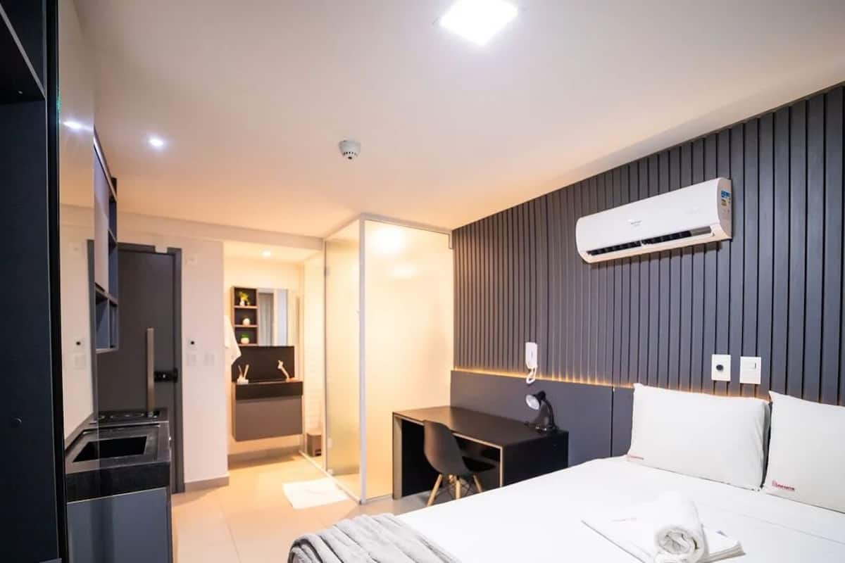 A modern hotel room with a bed, desk, and kitchenette.