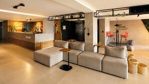 A modern reception area with a wooden reception desk, a sofa, and a seating area with red chairs. - Get One (Joao Pessoa)