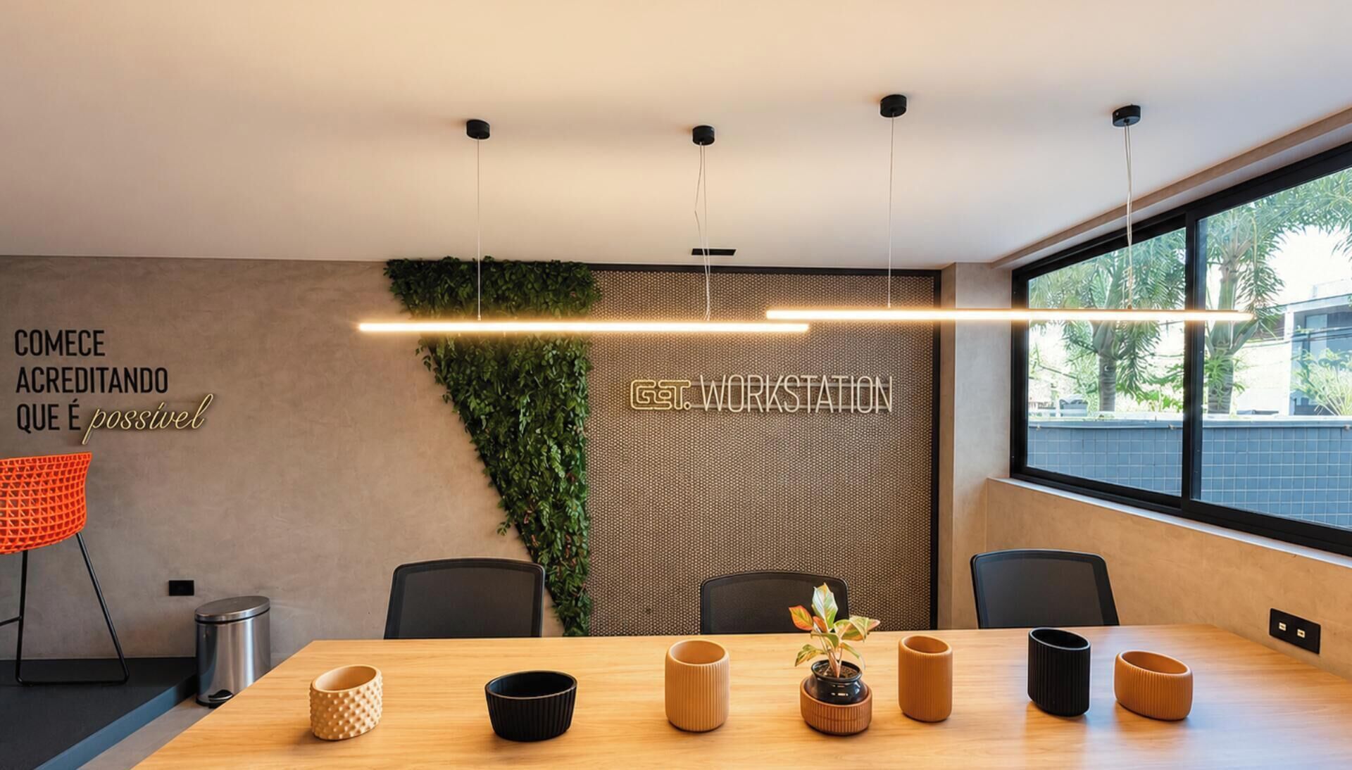A modern conference room with a long table, chairs, a potted plant, and a wall with a motivational quote.