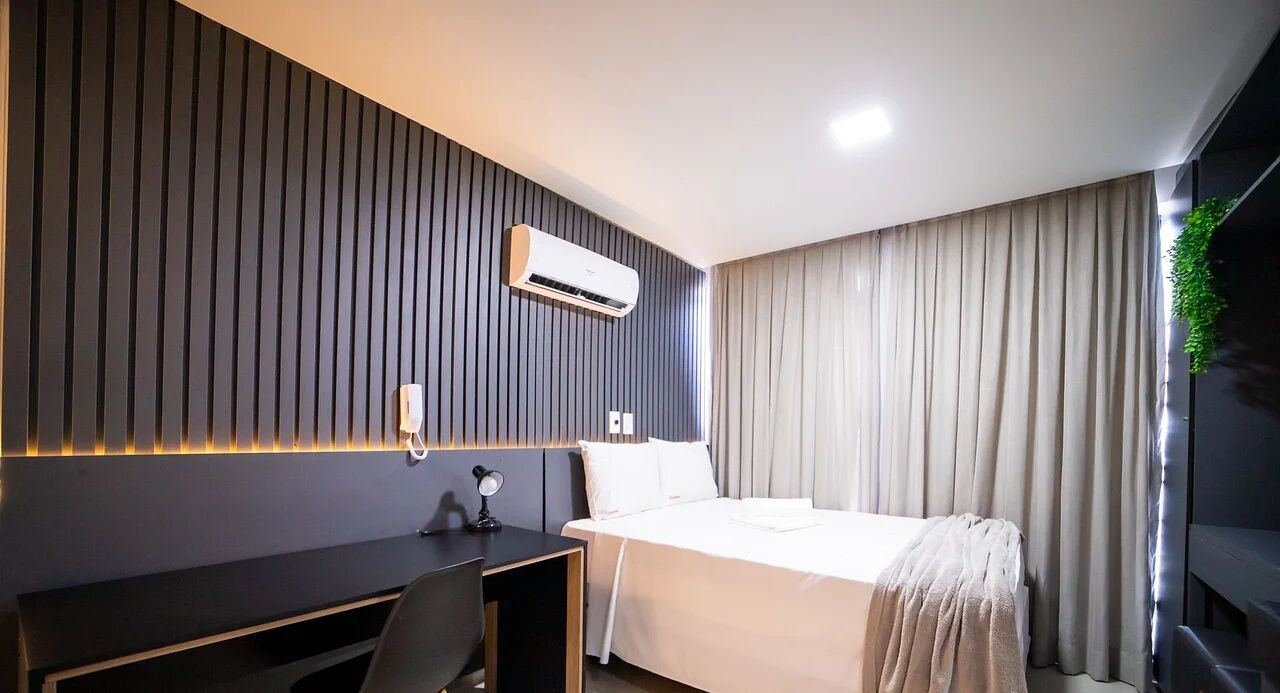 A modern hotel room with a bed, a desk, and an air conditioning unit.