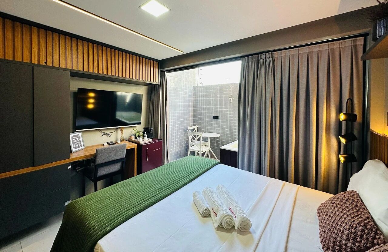 A hotel room with a bed, a desk, a chair, a television, and a window with curtains.