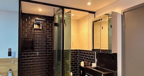 A modern bathroom with a black brick wall, a glass shower enclosure, and a large mirror.