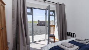 Un dormitorio con cama, una silla y vistas al exterior por una puerta de cristal.