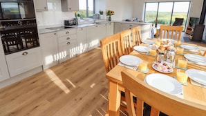 Una cocina moderna con armarios blancos, horno integrado y una zona de comedor con sillas de madera y una mesa dispuesta para el desayuno.