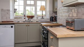 A kitchen with a built-in oven, a stovetop, a sink, and a window with a view of greenery. - 2 Beck Houses (Malton)