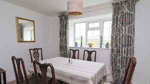A dining room with a table set for four, wooden chairs, a mirror, patterned curtains, and a window with a view of greenery. - 2 Beck Houses (Malton)