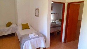 A small, clean room with two single beds, a wooden door, and a small bathroom visible through an open door. - cabañas puertas del sol (La Rioja)