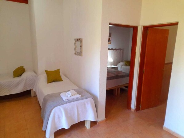 A small, clean room with two single beds, a wooden door, and a small bathroom visible through an open door.
