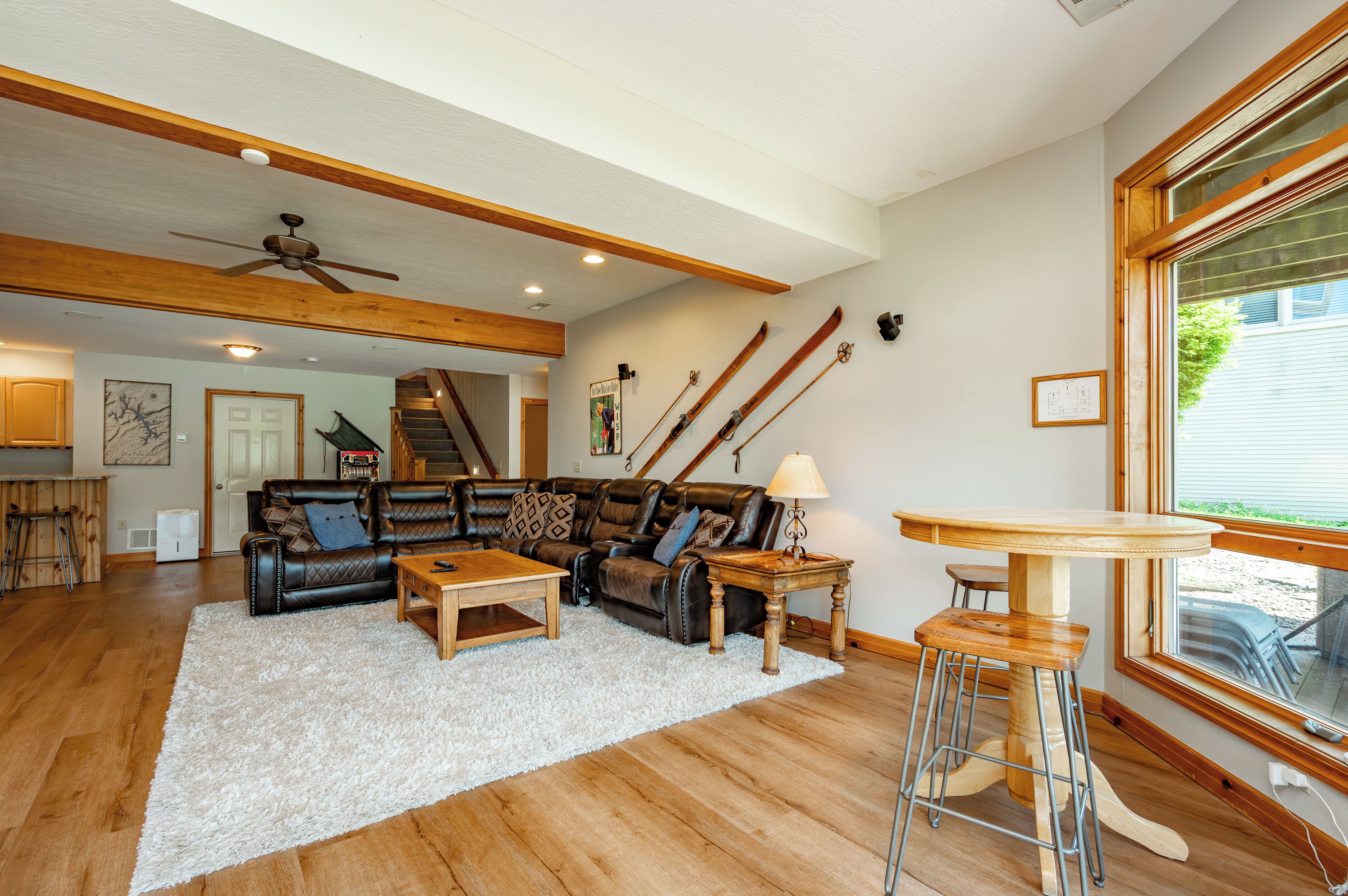 Un salon spacieux avec un grand canapé, une table basse et une table à manger. Un escalier mène à un autre niveau, et un porte-skis est fixé au mur.