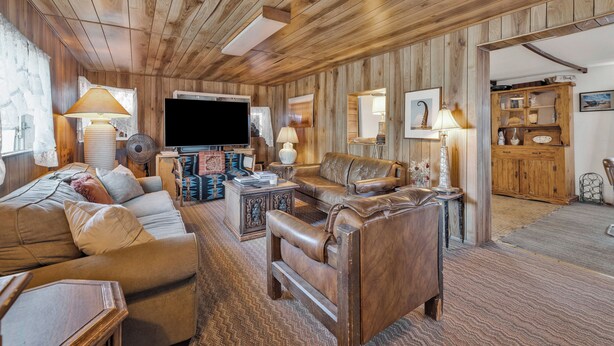 Een gezellige woonkamer met houten lambrisering, een grote flatscreen televisie, leren banken en een houten kast.