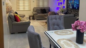 Una sala de estar moderna con zona de comedor, que incluye un sofá, una mesa de centro y un televisor montado en la pared.