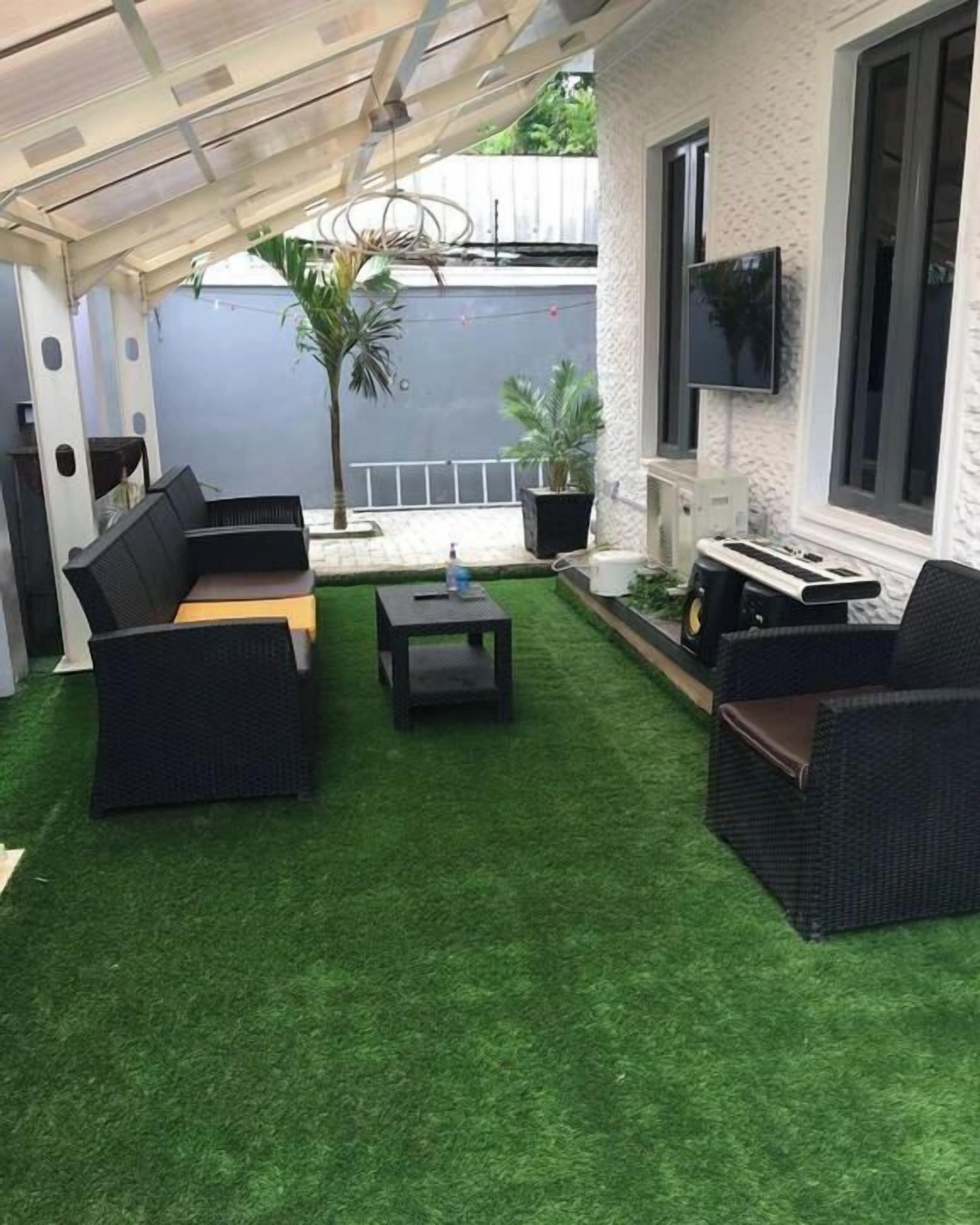 Een terras met kunstgras, zwart rieten meubilair en een flatscreen televisie aan de muur.