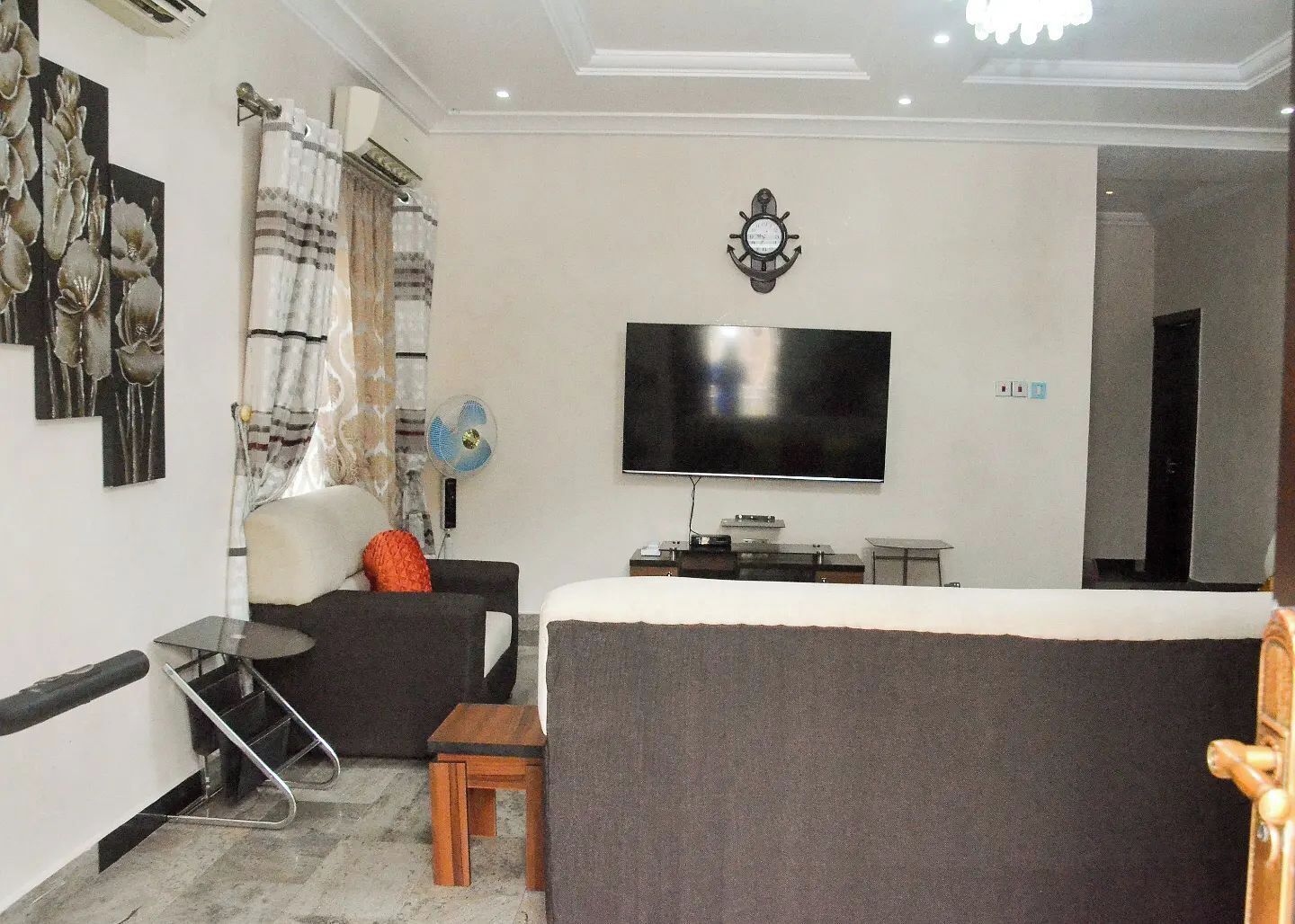 A living room with a flat-screen TV, a sofa, a small table, and a fan.