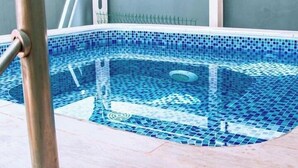 Una piscina con mosaicos azules, una escalera metálica y un área techada.