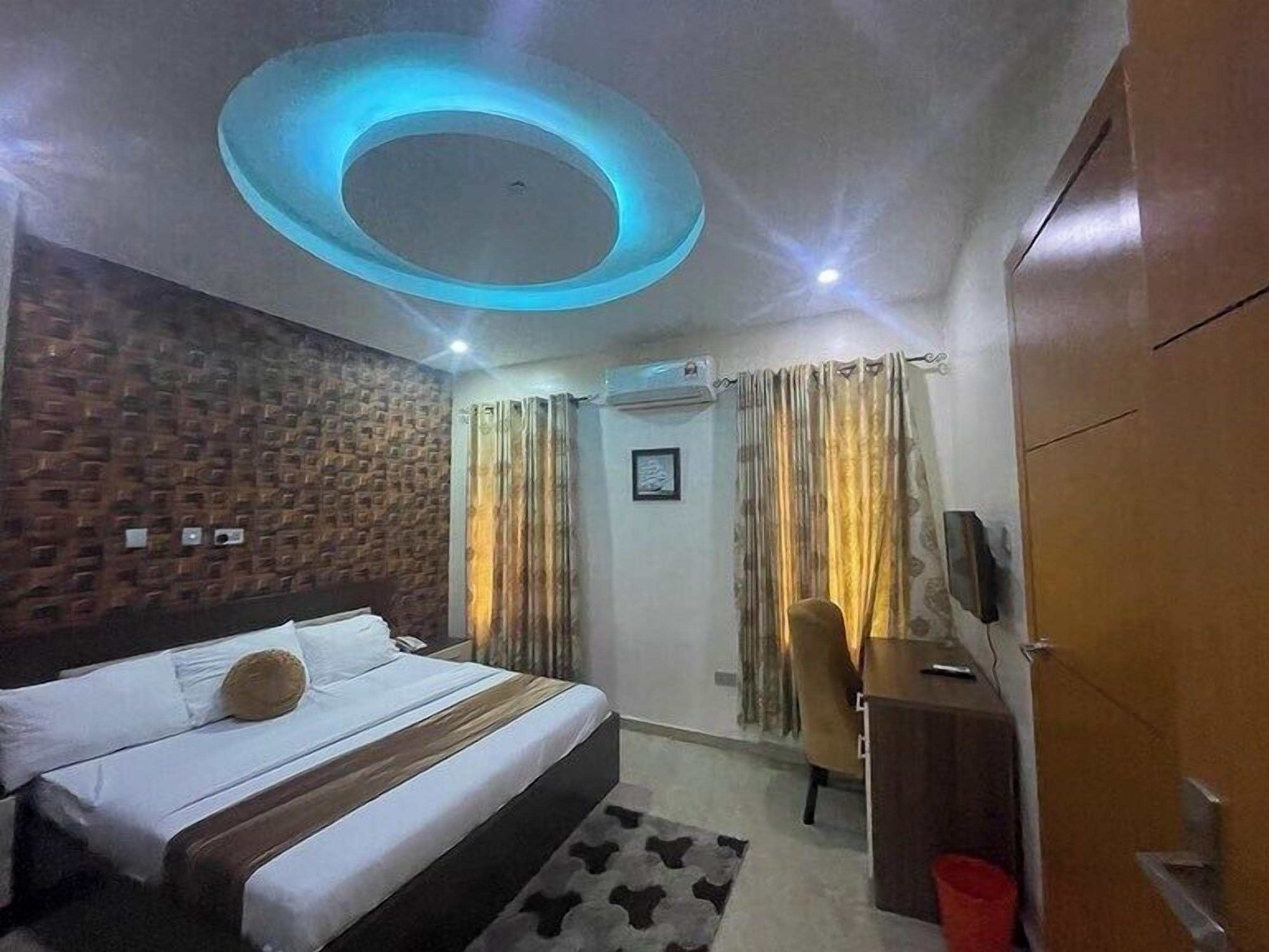 A hotel room with a bed, a desk, a chair, a TV, and a ceiling light fixture.