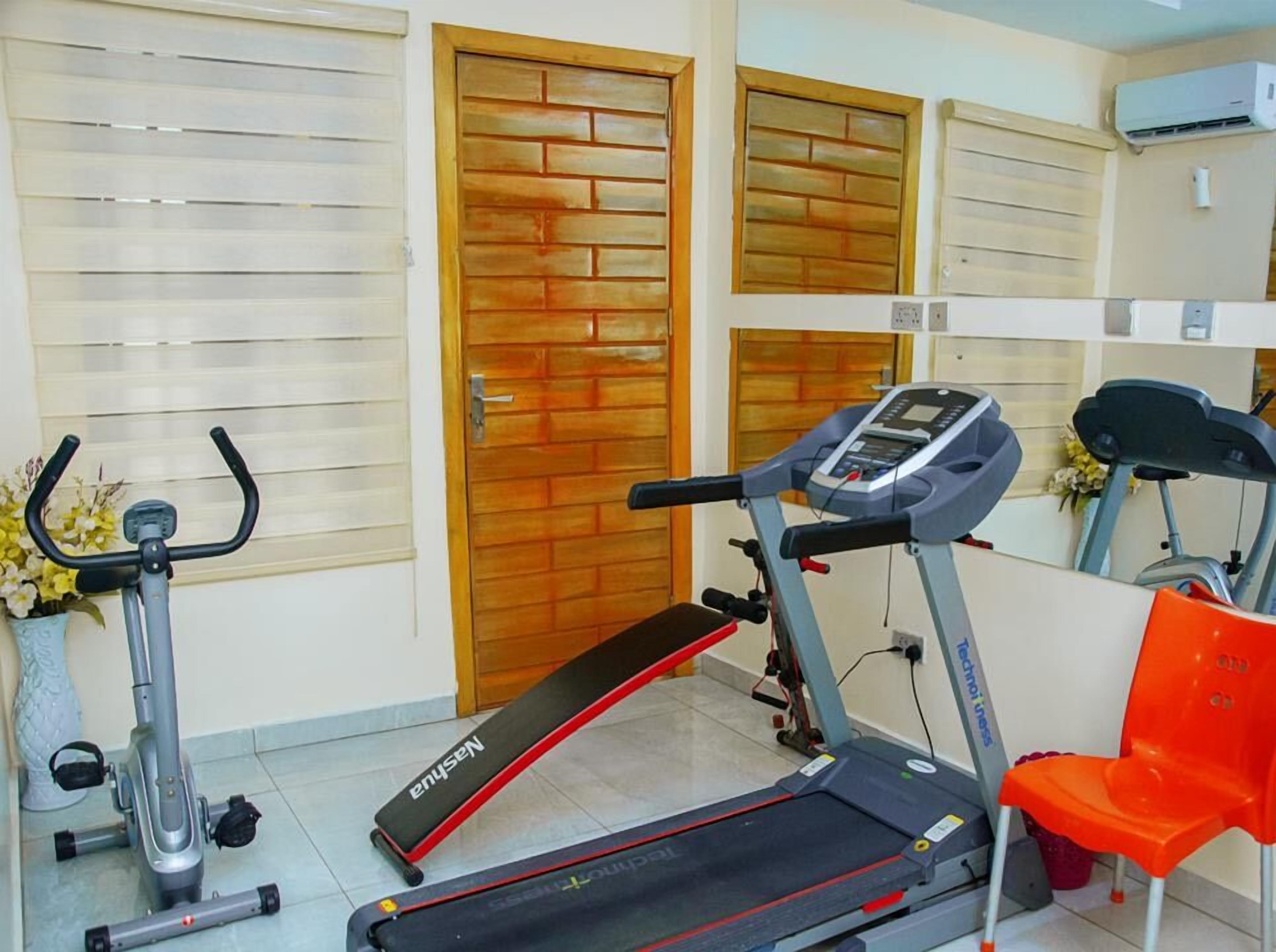 Een fitnessruimte met loopbanden, een hometrainer en een rode stoel.