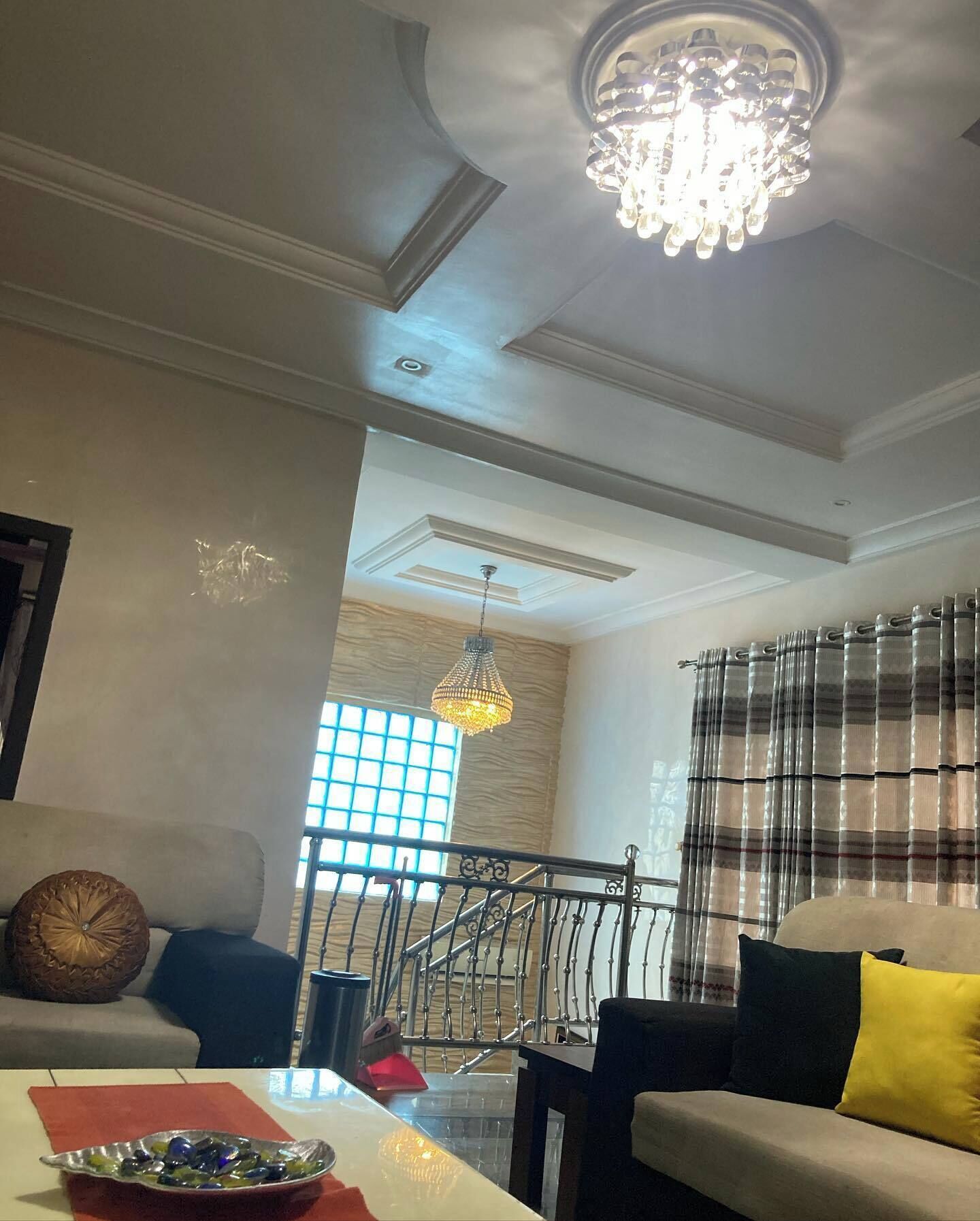 Uma sala de estar com um lustre, uma escadaria e vista para o exterior.