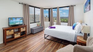 A hotel room with a large bed, a TV on a wooden console, a sofa, and a view of the city. - Awesome view. Walking distance to beach, restaurants, shopping (Honolulu)