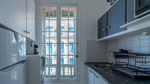 Una cocina compacta con armarios blancos, un horno integrado y un ventanal con vistas a edificios.