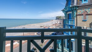 Vista costera desde un balcón con cielo despejado, una playa y un edificio con detalles azules.