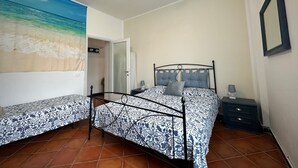 A bedroom with a bed, a ceiling fan, a nightstand, and a wall with a beach mural. - Chiaraluce Monte Cosy Apt near best beaches (Monterosso al Mare)