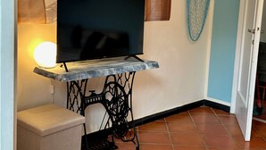 A television on a metal stand with a power outlet, a small stool, and a decorative wall hanging. - Chiaraluce Monte Cosy Apt near best beaches (Monterosso al Mare)
