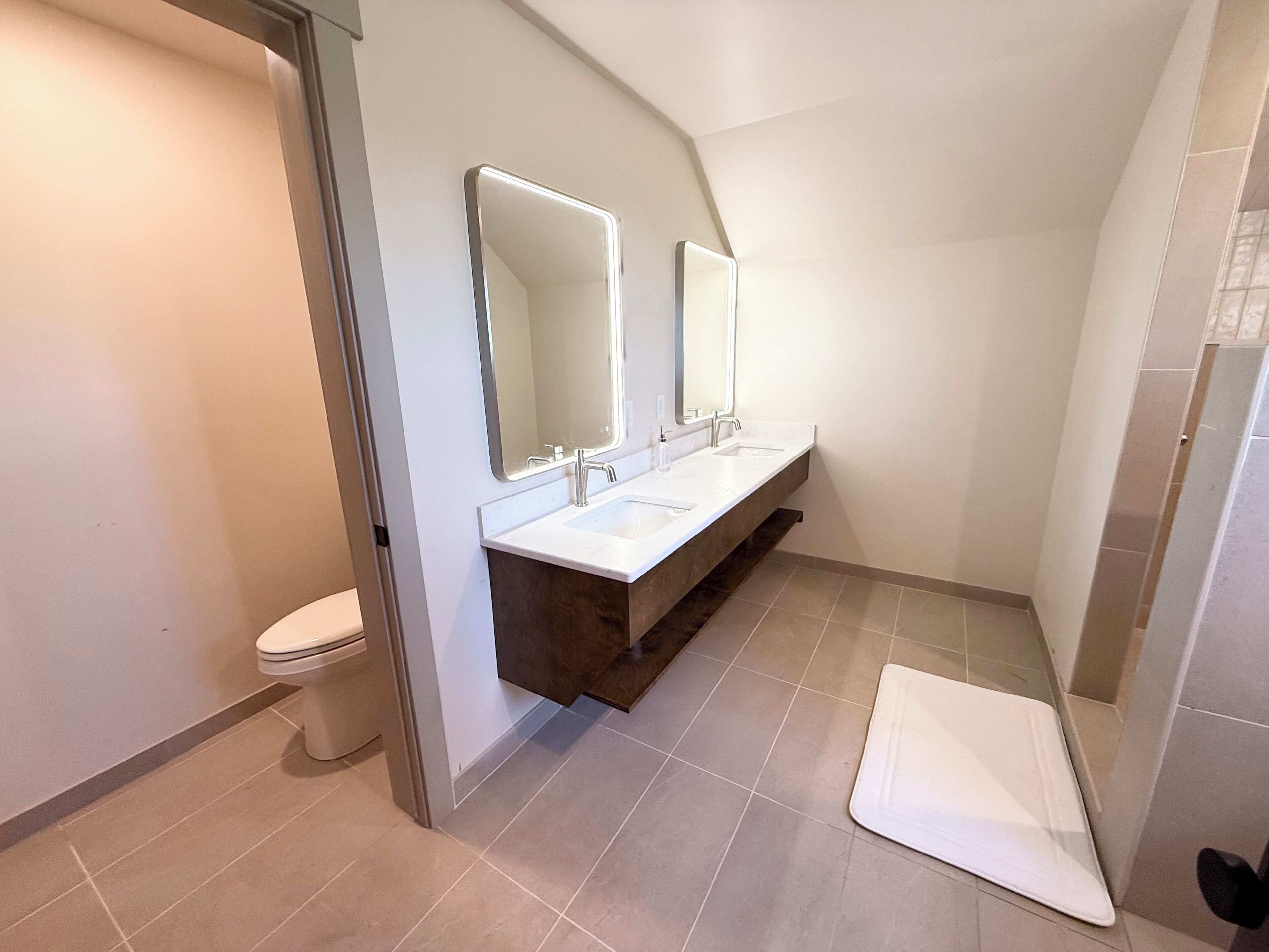 A modern bathroom with two sinks, a toilet, and a shower area.
