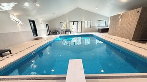 Una piscina interior con agua azul cristalina, suelo de baldosas y una larga escalera blanca.
