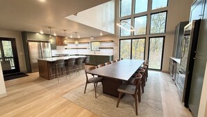 Una cocina moderna con una isla grande, mesa de comedor de madera y abundante luz natural proveniente de amplias ventanas.