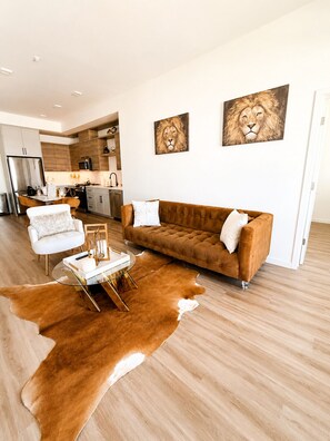 Una sala de estar moderna con un sofá marrón, sillones blancos, una mesa de centro de vidrio y una alfombra de cuero de vaca.