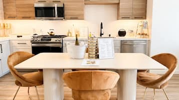 Cozinha moderna com armários de madeira, eletrodomésticos de aço inoxidável e uma mesa de jantar branca com duas cadeiras.