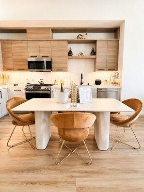 Una cocina moderna con armarios de madera, electrodomésticos de acero inoxidable y una mesa de comedor blanca con dos sillas.